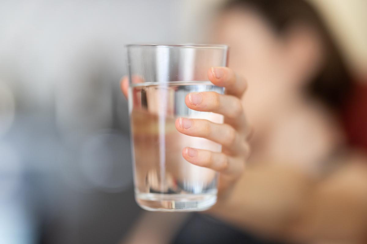 A person holding a glass of water and drinking it