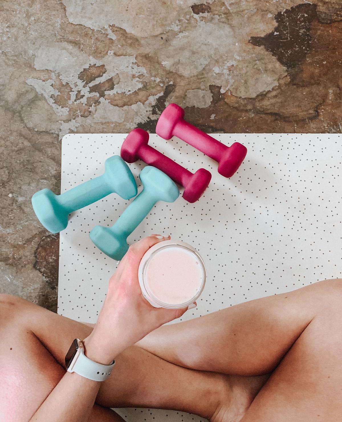 A person setting fitness goals with a notebook and pen, with dumbbells and a water bottle beside them